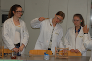 3 Schülerinnen experimentieren mit einem Bunsenbrenner